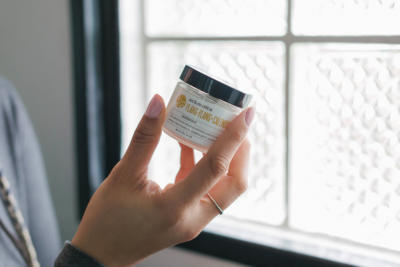 Woman's hand holding Schmidt's ylang ylang and calendula jar deodorant against backdrop of window